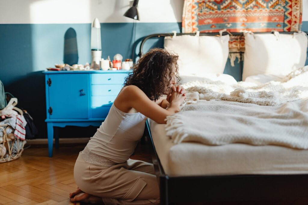 Woman praying kneeling at a bed