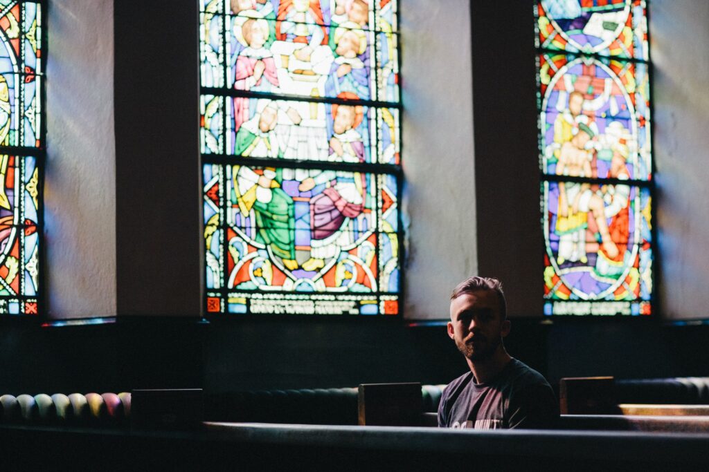 Man sitting in a church with stained glass windows.