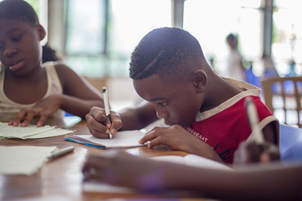 A school-aged boy wearing a red shirtfocuses on his homework