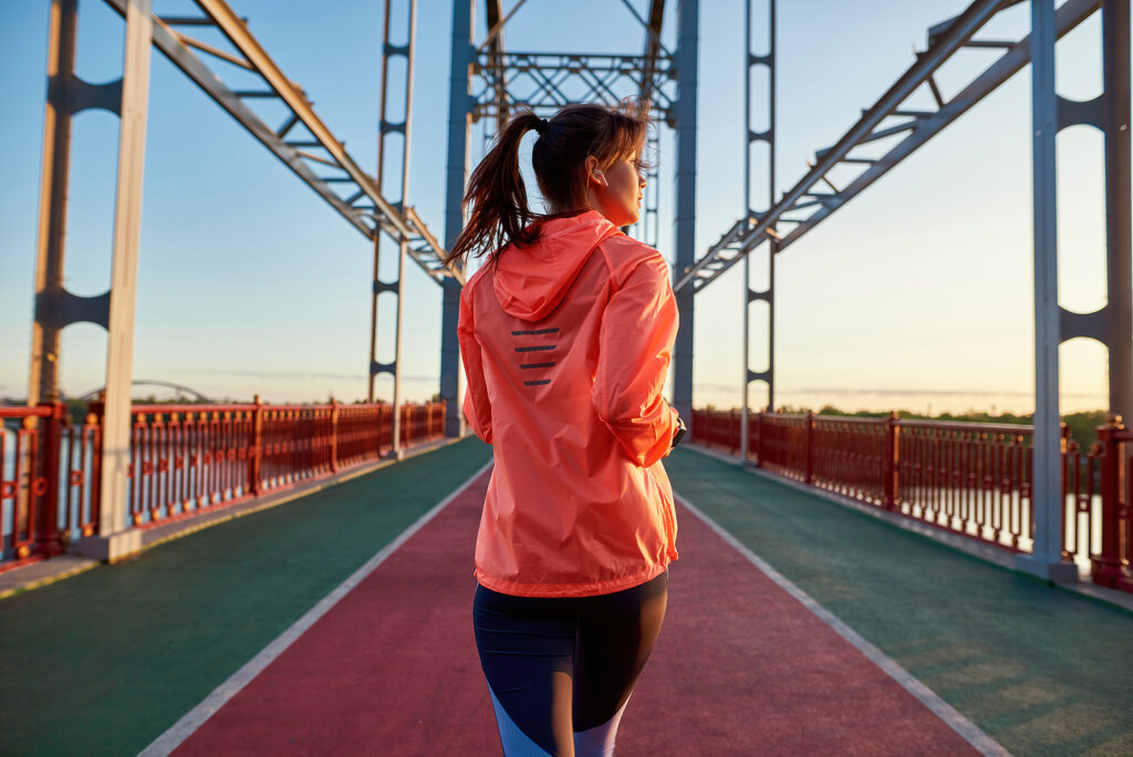 Woman in a pink jacket runs on a bridge at sunset.