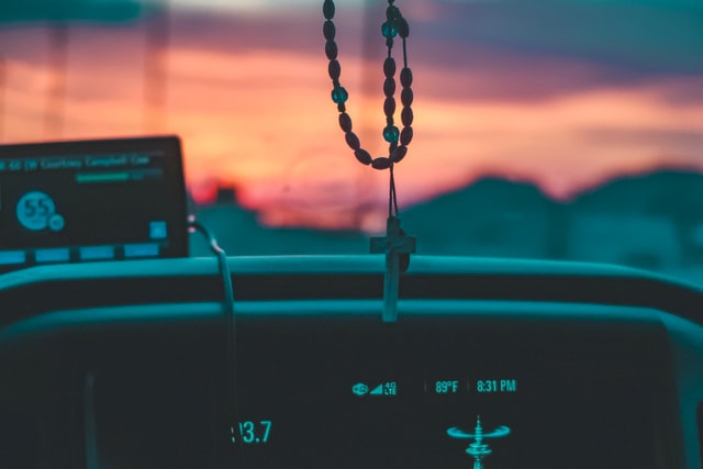 Image of a rosary hanging in front of a car windshield at dusk.