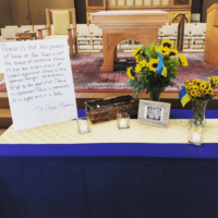 A table before the altar, decorated with flowers and a prayer for peace in Ukraine.