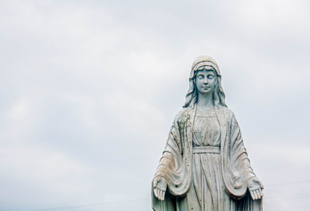 A statue of the blessed virgin against an overcast sky