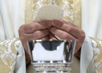 A priest hold the Eucharist above a silver chalice.