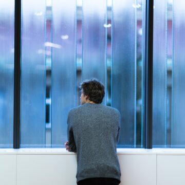 Man standing and facing a glass wall.