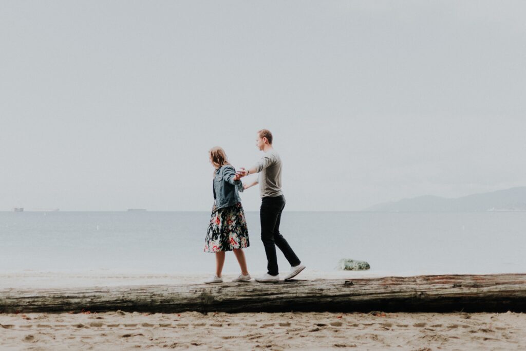 A man guides a woman on a cloudy, gray beach near the ocean.