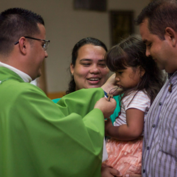 Priest in Ordinary Time vestments blessing a young girl with her parents.
