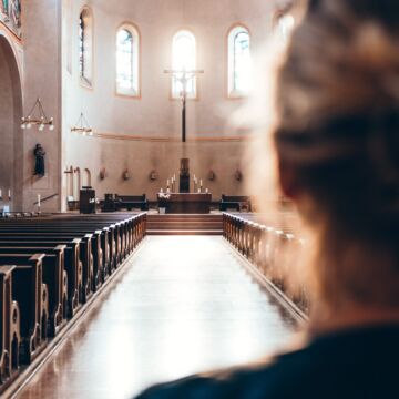 Blurred photo of a woman looking down the center aisle of a church.