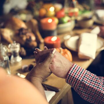 Family members holding hands around a table for a Thanksgiving feast
