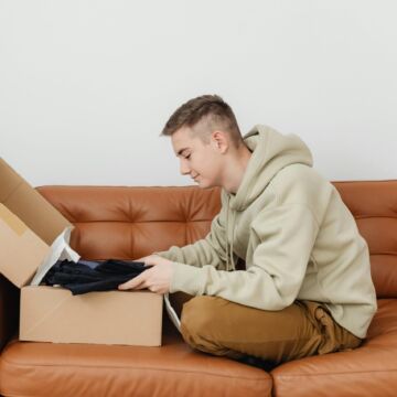 Young man sitting on orange couch opening a cardbox box